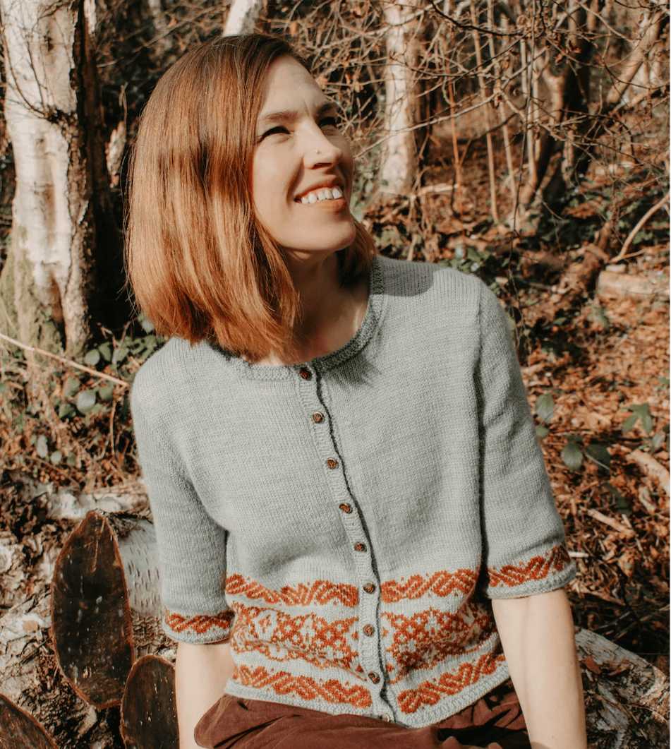 Zanete wearing the Ailis Sweater as a cardigan in pale sage with burnt-orange Latvian colourwork at the hem
